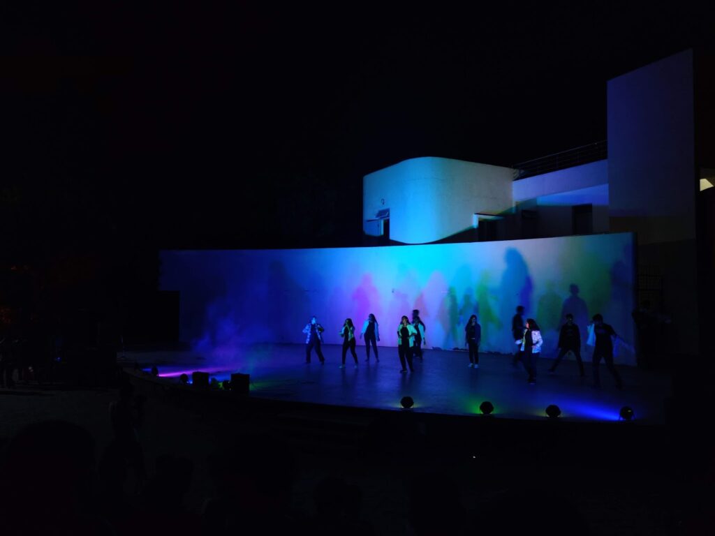 A distance capture of a dance happening in the open-air amphitheater. The stage is lit up and the lights are focussed on the dancers, with the surroundings in darkness