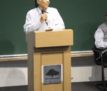 A picture of Prof. PJ Naraynan standing by a lectern, giving his last speech as a Director