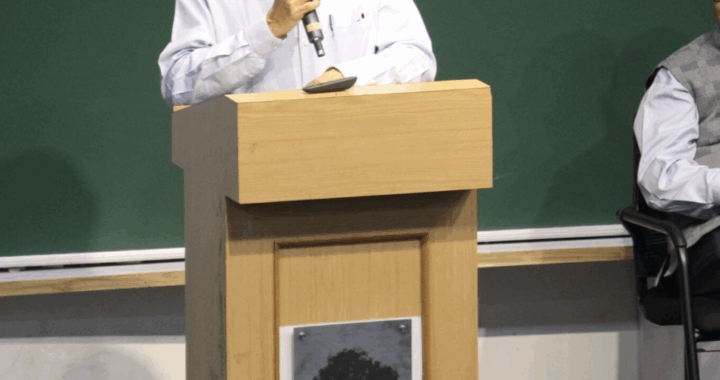 A picture of Prof. PJ Naraynan standing by a lectern, giving his last speech as a Director